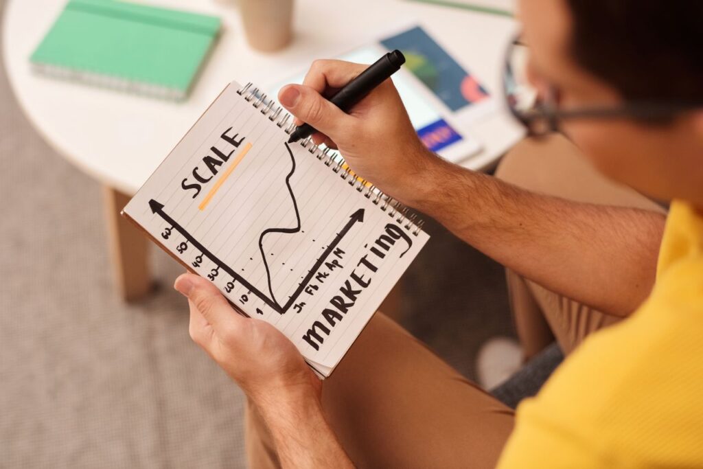pexels photo 6476777 6476777 Close-up of a man drawing a marketing strategy graph in a notebook.